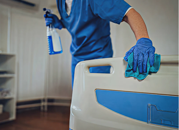 Worker in protective gloves cleaning a surface with a cloth and spray bottle, illustrating sanitation practices in a healthcare setting.