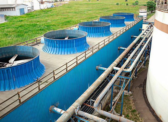 Industrial cooling towers with blue structures and connected pipes, set in a grassy area, illustrating water management infrastructure.