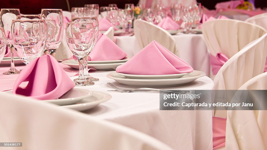 Elegant table setting with pink napkins and glassware arranged on white tablecloths, suggesting a formal dining or event setup.