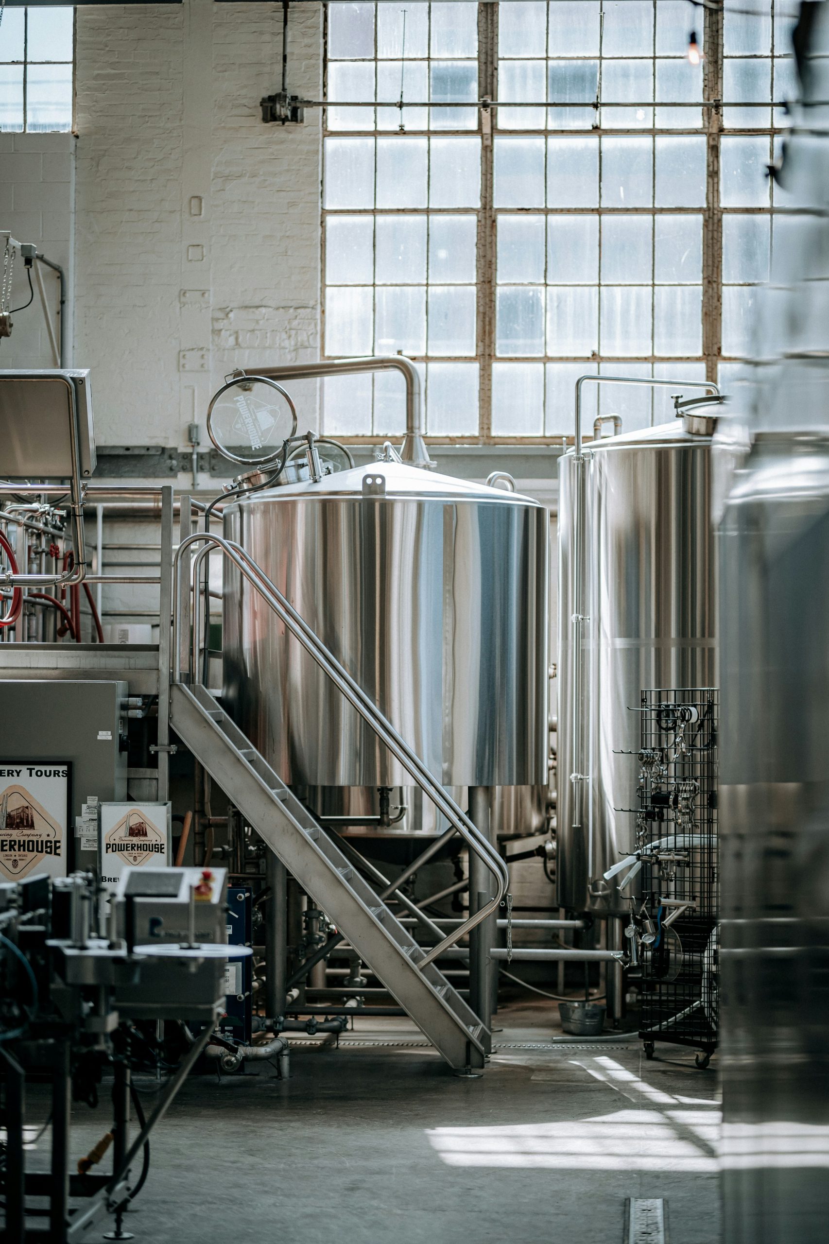 Stainless steel brewing tanks in a sunlit industrial facility, highlighting equipment used in beverage production.