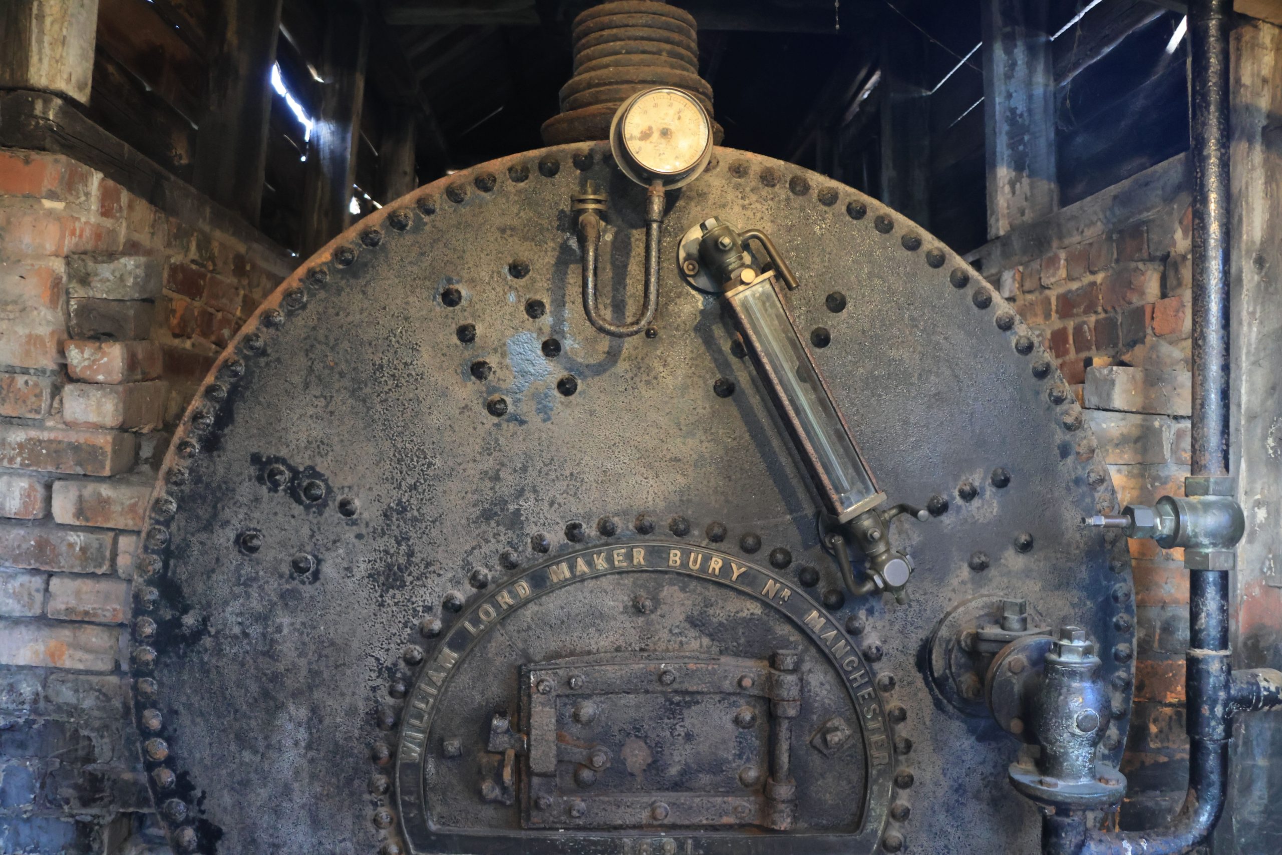 Industrial boiler with pressure gauge and rusted metal surface, set against a brick wall, illustrating water management solutions.