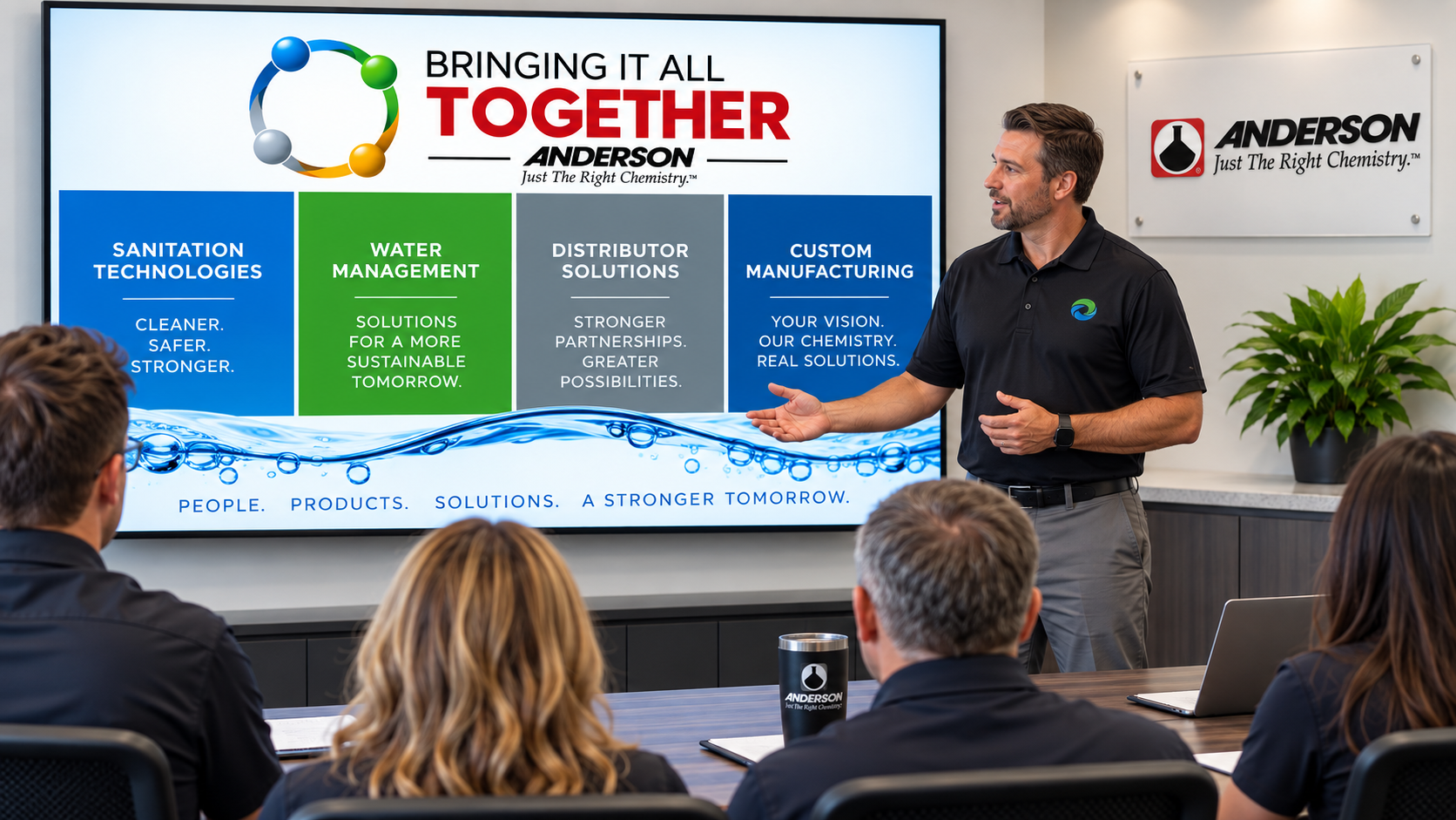 Presenter in a meeting room discussing Anderson Chemical Company's four divisions: Sanitation Technologies, Water Management, Distributor Solutions, and Custom Manufacturing, with a focus on partnerships and innovative solutions.