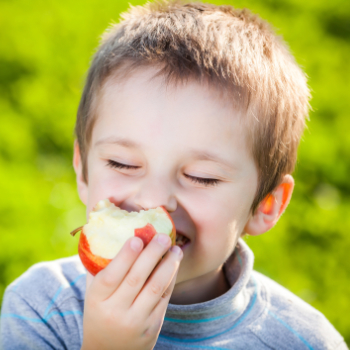 Child smiling while eating an apple outdoors, highlighting the importance of fresh produce in a healthy diet.