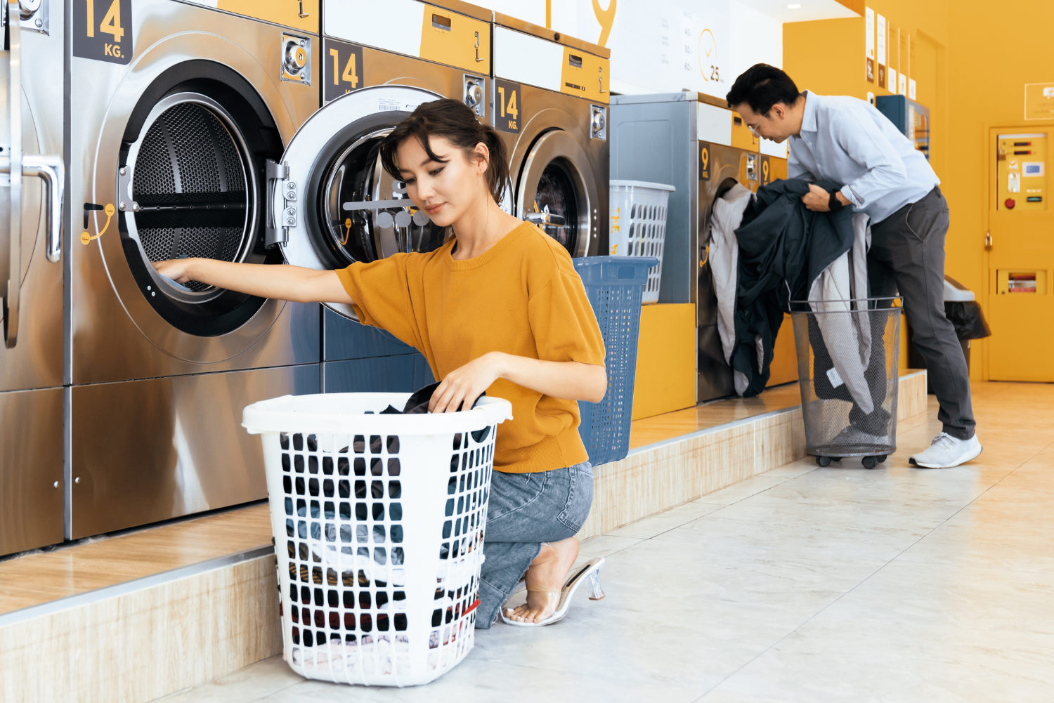Person using a coin-operated laundry machine in a public laundromat, placing clothes into a basket.