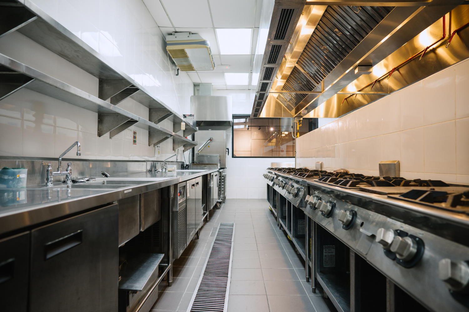 Commercial kitchen with stainless steel appliances, including stoves and sinks, emphasizing cleanliness and efficiency.