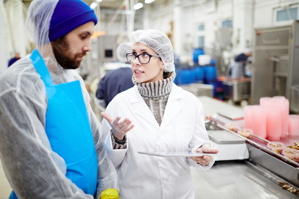 Fish factory expert with a touchpad discussing improved working conditions with a worker, highlighting sanitation solutions.