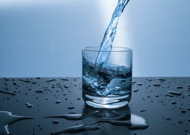 Water being poured into a glass, surrounded by droplets on a reflective surface, illustrating clean and efficient water management.